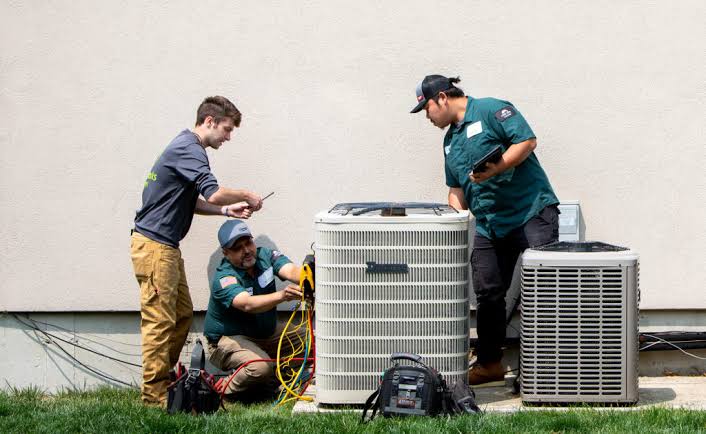 Three HVAC technicians inspecting residential outdoor cooling equipment