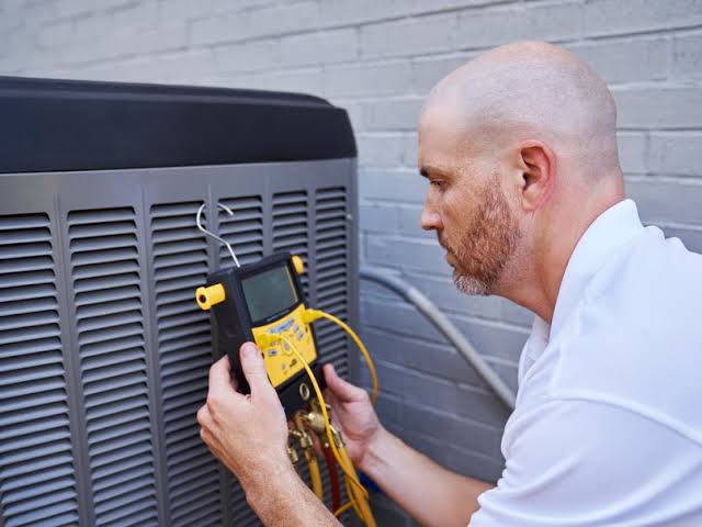 Technician using a yellow diagnostic meter to inspect an outdoor HVAC unit