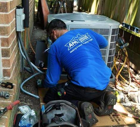 Technician in a blue shirt servicing an outdoor air conditioner beside a brick wall